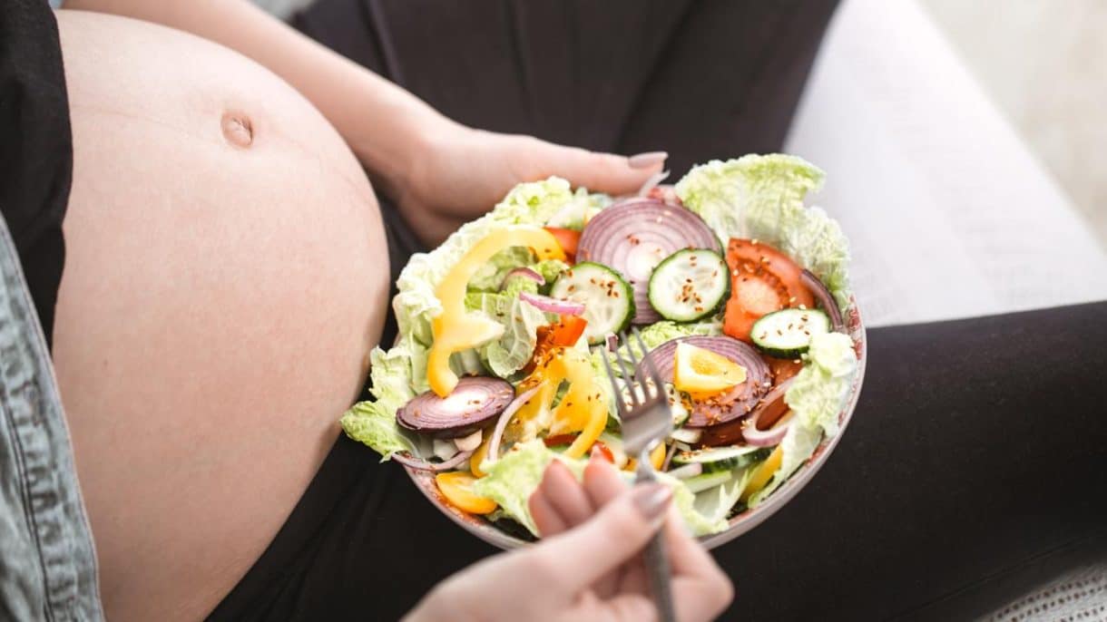 mujer embarazada feliz comiendo comida vegana saludable