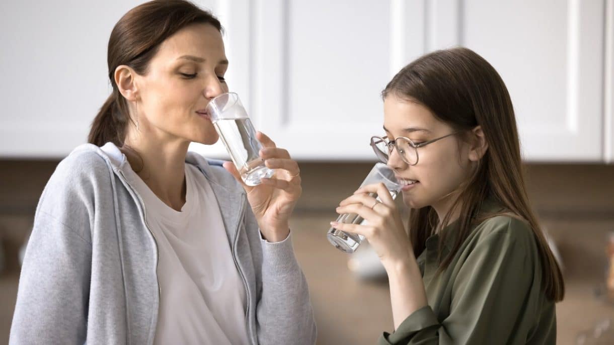 Mujer bebiendo agua para cumplir con la recomendación de beber dos litros de agua al día.