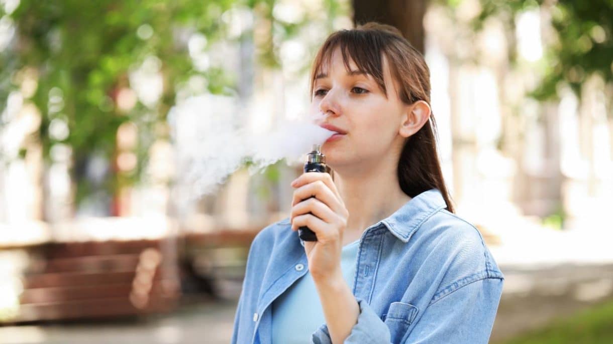 Joven vapeando al aire libre con un dispositivo electrónico.