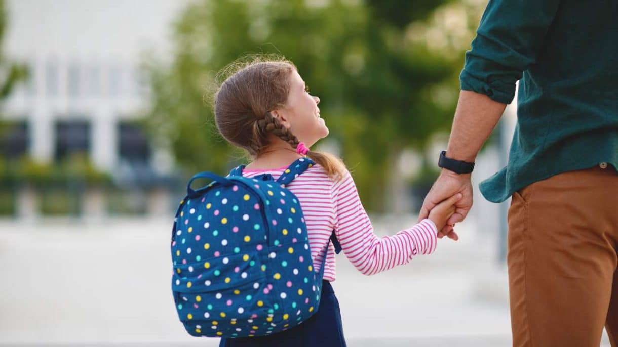 Niños entrando a la escuela con mochilas y padres acompañándolos