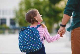 Niños entrando a la escuela con mochilas y padres acompañándolos