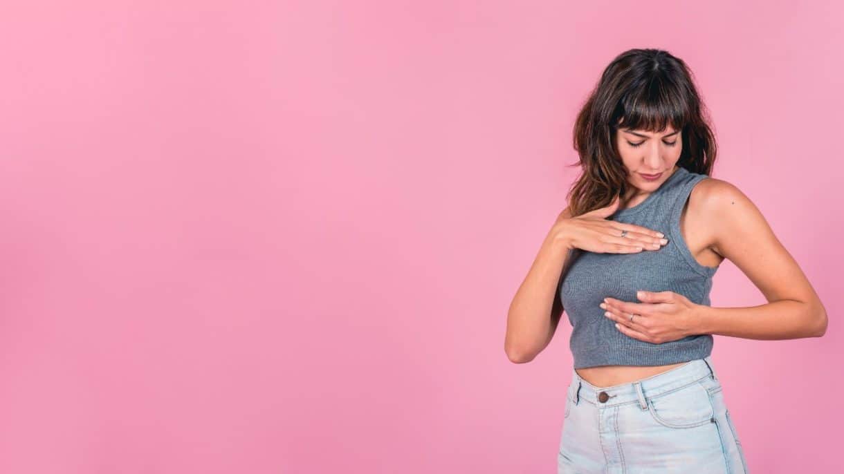 Mujer revisándose los senos con informe médico de cáncer de mama