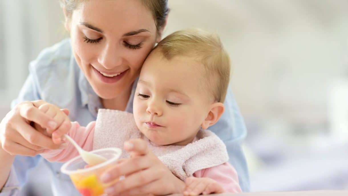 Madre alimentando a su bebé con frutas en casa mientras juegan 