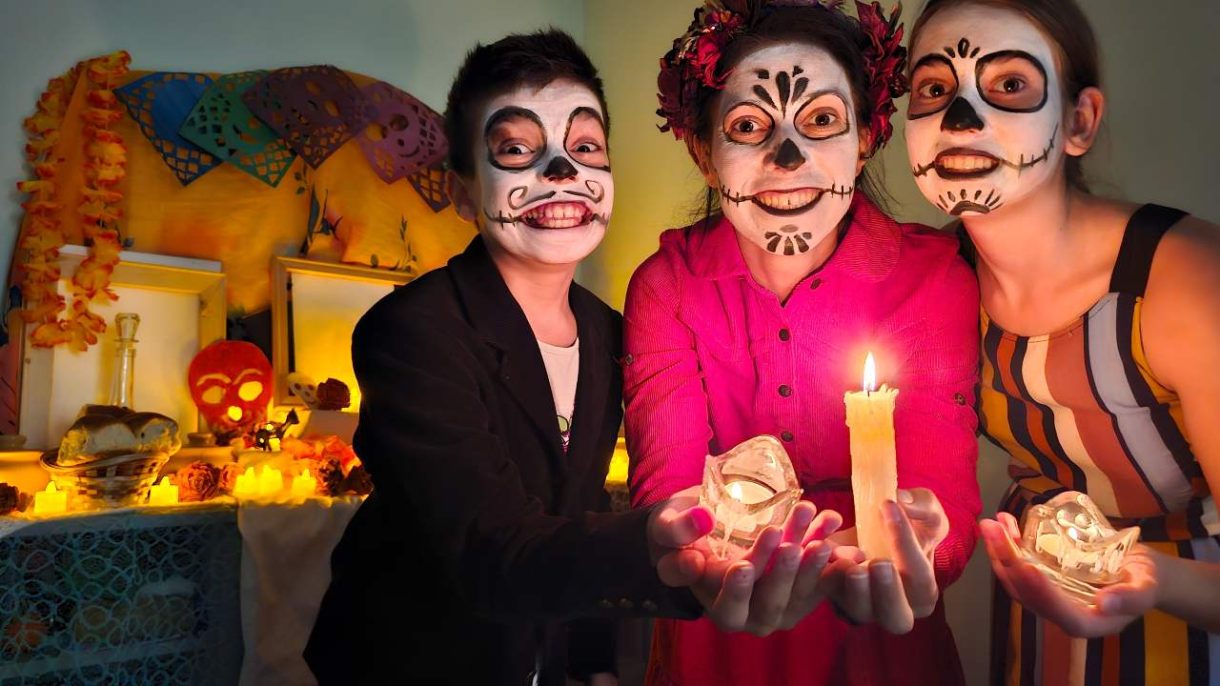 Familia sonriendo abrazados con decoración de Halloween y Día de Muertos en casa.