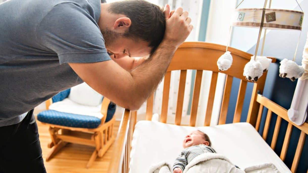 Padre con su bebé en brazos, con gesto de cansancio y reflexión.