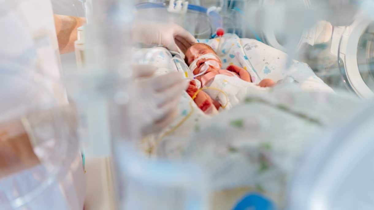 Bebé prematuro descansando dentro de una incubadora neonatal rodeado de monitores médicos.
