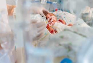 Bebé prematuro descansando dentro de una incubadora neonatal rodeado de monitores médicos.