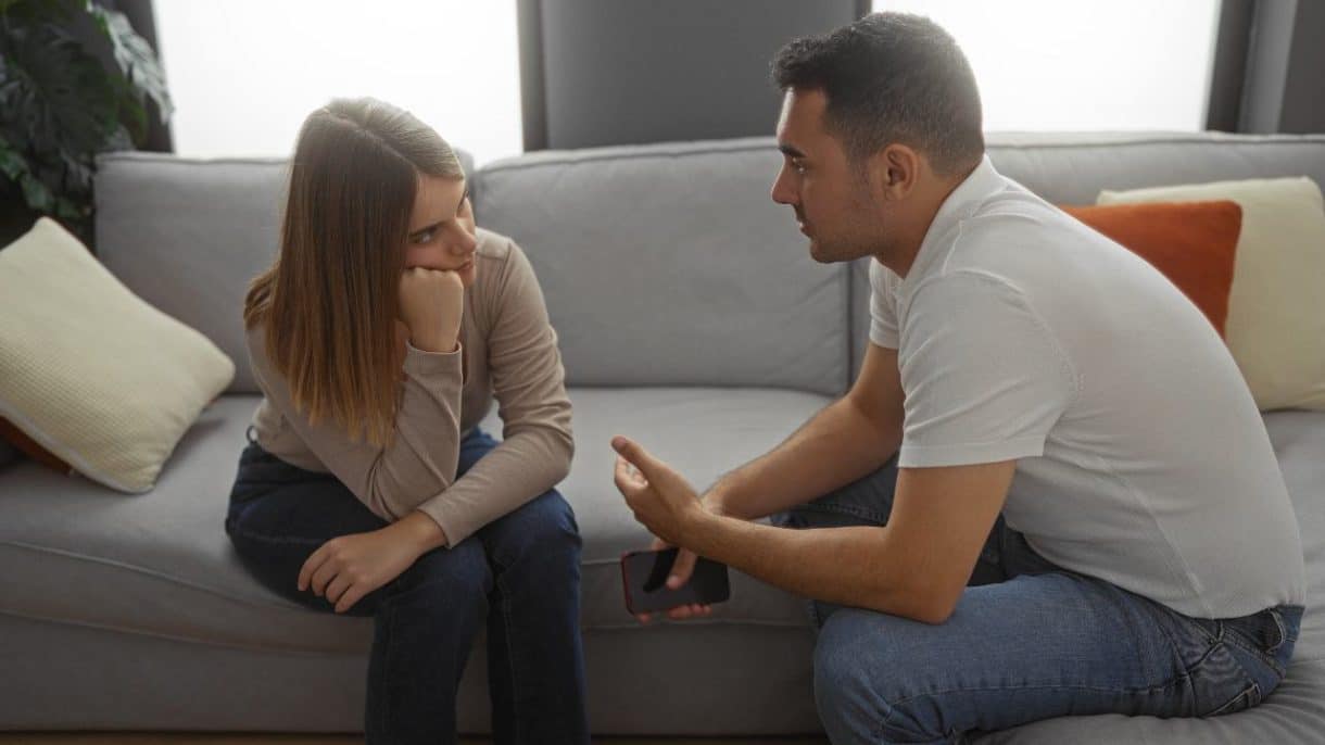 Pareja conversando seriamente en un sofá, mostrando una charla íntima y reflexiva.