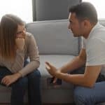 Pareja conversando seriamente en un sofá, mostrando una charla íntima y reflexiva.