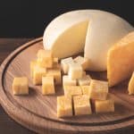 Variedad de quesos grasos como cheddar y brie sobre una tabla de madera.