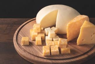 Variedad de quesos grasos como cheddar y brie sobre una tabla de madera.