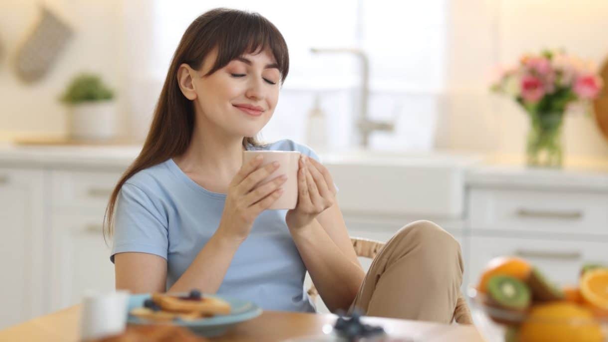 Persona sonriente sosteniendo una taza humeante, ilustrando los beneficios del consumo de café en la salud mental.