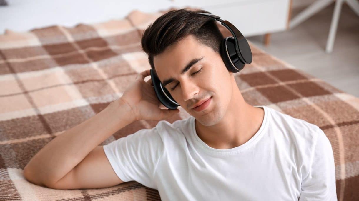 Persona joven escuchando música con auriculares con expresión reflexiva, ilustrando la relación entre estado de ánimo y música.