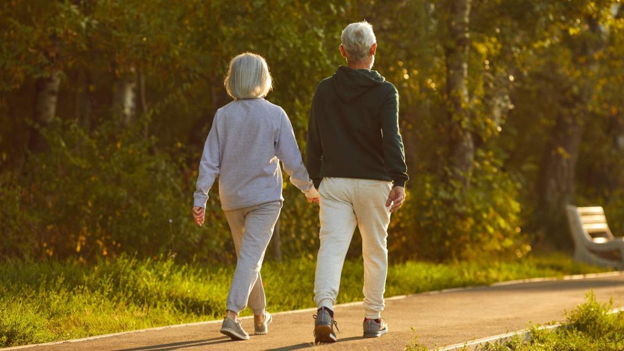 Una persona mayor caminando con paso firme por un sendero arbolado durante una mañana soleada, reflejando el beneficio del ejercicio para prevenir el Alzheimer.