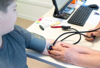 Un pediatra midiendo la presión arterial a un adolescente en una consulta médica, alertando sobre el aumento de la hipertensión pediátrica.