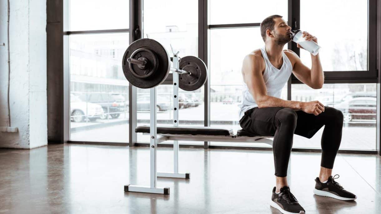 Batido de proteínas junto a una persona entrenando en el gimnasio