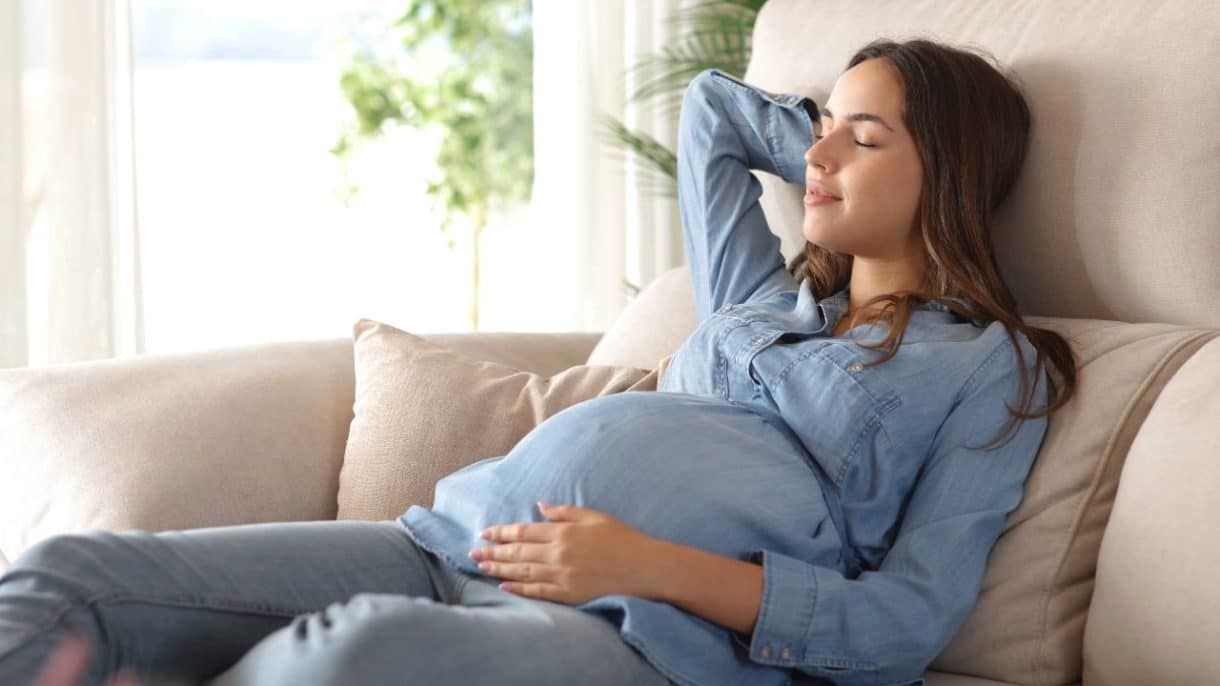 Mujer embarazada descansando en un interior fresco durante un día caluroso, representando la importancia de la protección térmica para la salud gestacional.