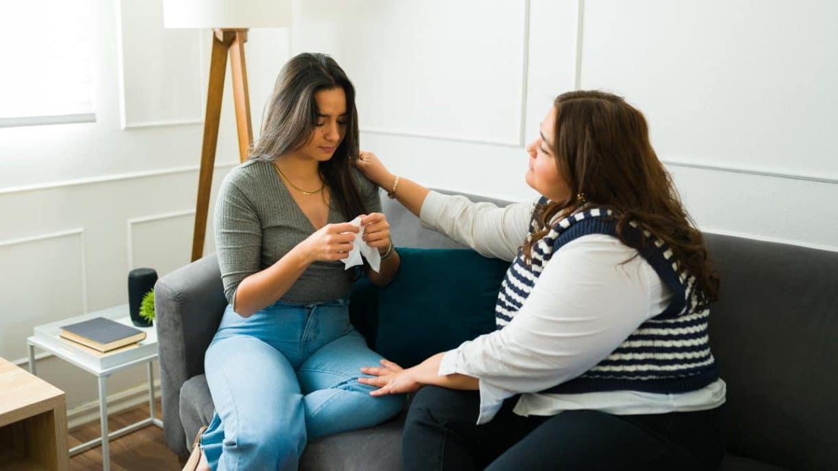 Mujer acompañando en silencio a una amiga triste mientras conversan en un sofá.